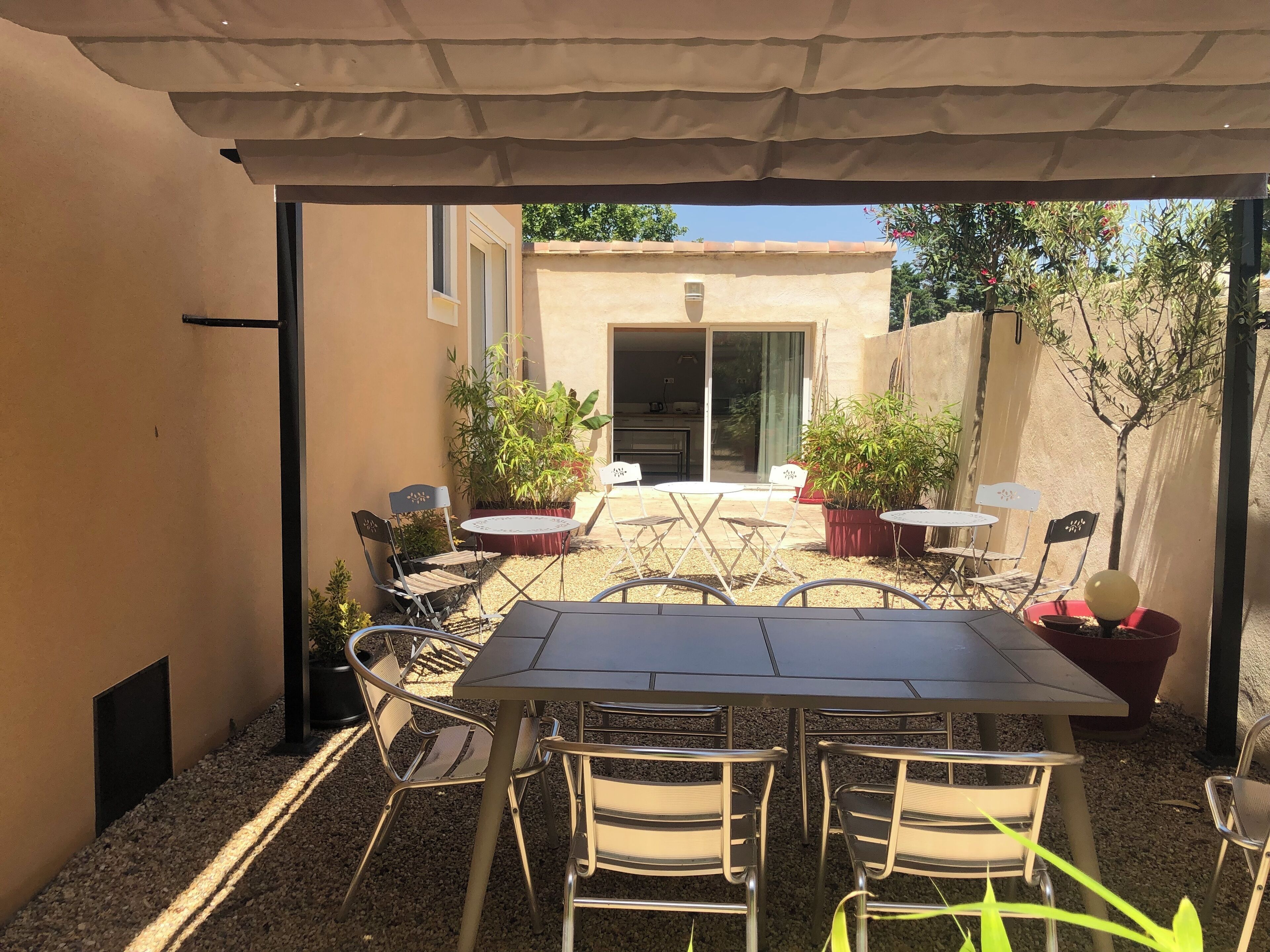 A covered patio with a table and chairs, surrounded by potted plants and a view of a building.
