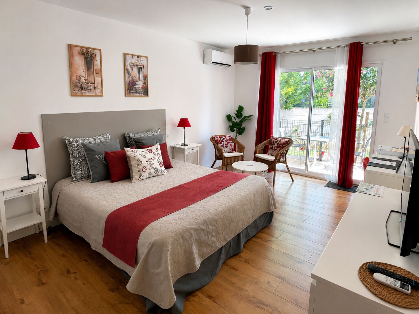 Een moderne hotelkamer met een groot bed, twee nachtkastjes, een bureau met een stoel, een balkon met rode gordijnen en kunst aan de muren.