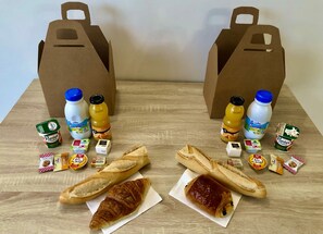 A table with two paper bags, two bottles of juice, two containers of yogurt, and various snacks and bread. - Lou Meinado (Saint-Martin-de-Crau)