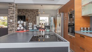A modern kitchen with a central island, stainless steel appliances, and a view of the city. - Villa Parisi Naxos Deluxe 1 (Agkidia)