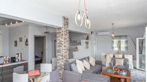 A modern living room with a grey sofa, a glass coffee table, and a dining area with a red tablecloth. - Villa Parisi Naxos Deluxe 1 (Agkidia)