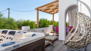 A hot tub with controls, a hanging chair, and a covered seating area with a table and chairs. - Villa Parisi Naxos Deluxe 1 (Agkidia)