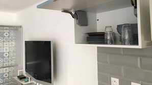 A kitchen with a built-in TV, a shelf with plates and glasses, and a patterned backsplash. - Studio cabin 4 beds, sea view: beach 5 min + parking + air conditioning (Mauguio)