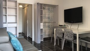 A modern living room with a grey sofa, a dining table with chairs, a TV mounted on the wall, and a walk-in closet with patterned tiles. - Studio cabin 4 beds, sea view: beach 5 min + parking + air conditioning (Mauguio)