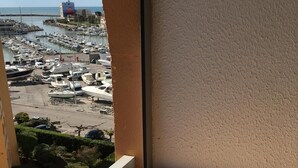 A balcony with a wooden table and a view of a marina with boats and a building in the distance. - Studio cabin 4 beds, sea view: beach 5 min + parking + air conditioning (Mauguio)