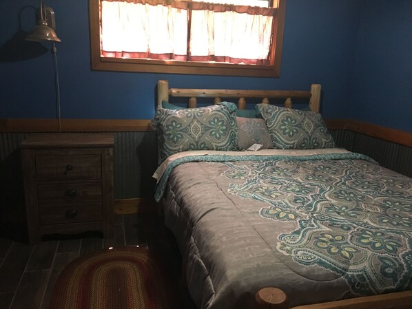 Un dormitorio con una cama, una mesita de noche, una lámpara y una ventana con cortinas.