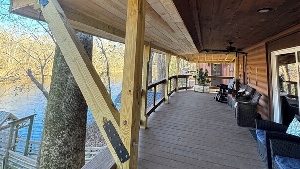 Una terraza de madera con barandilla, mobiliario exterior y vista a un lago.