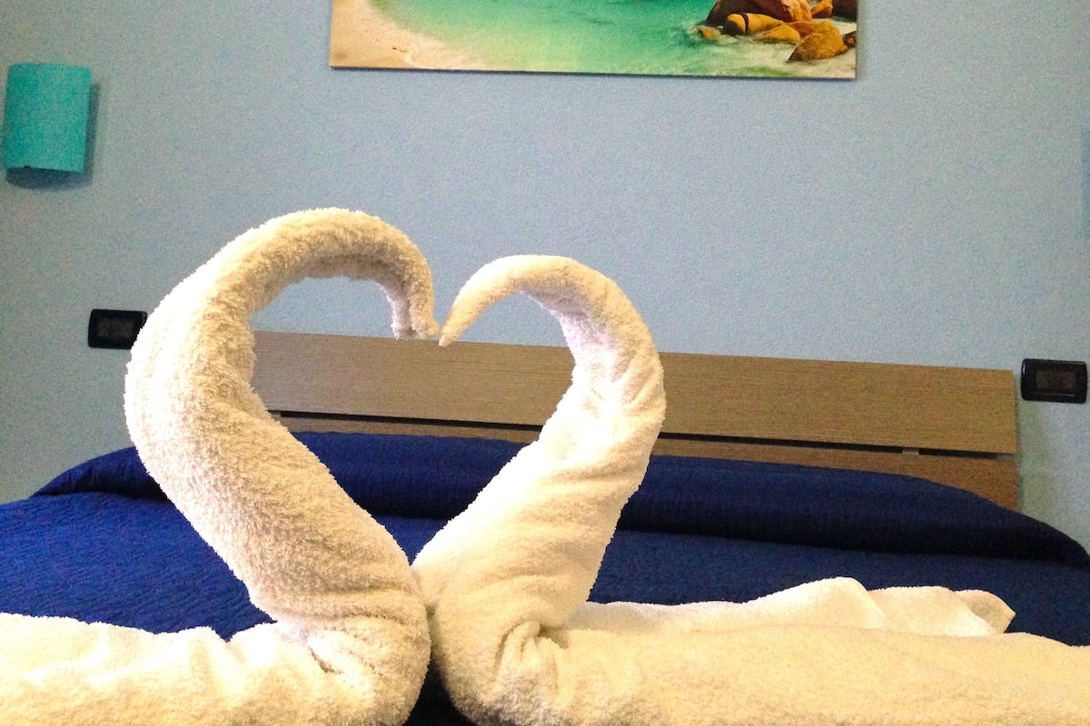 A bed with a blue bedspread and two white towels arranged in a heart shape.