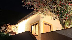 A building with a lighted entrance, a window, and a tree with pink flowers. - Villa Verdesca (San Vito Lo Capo)