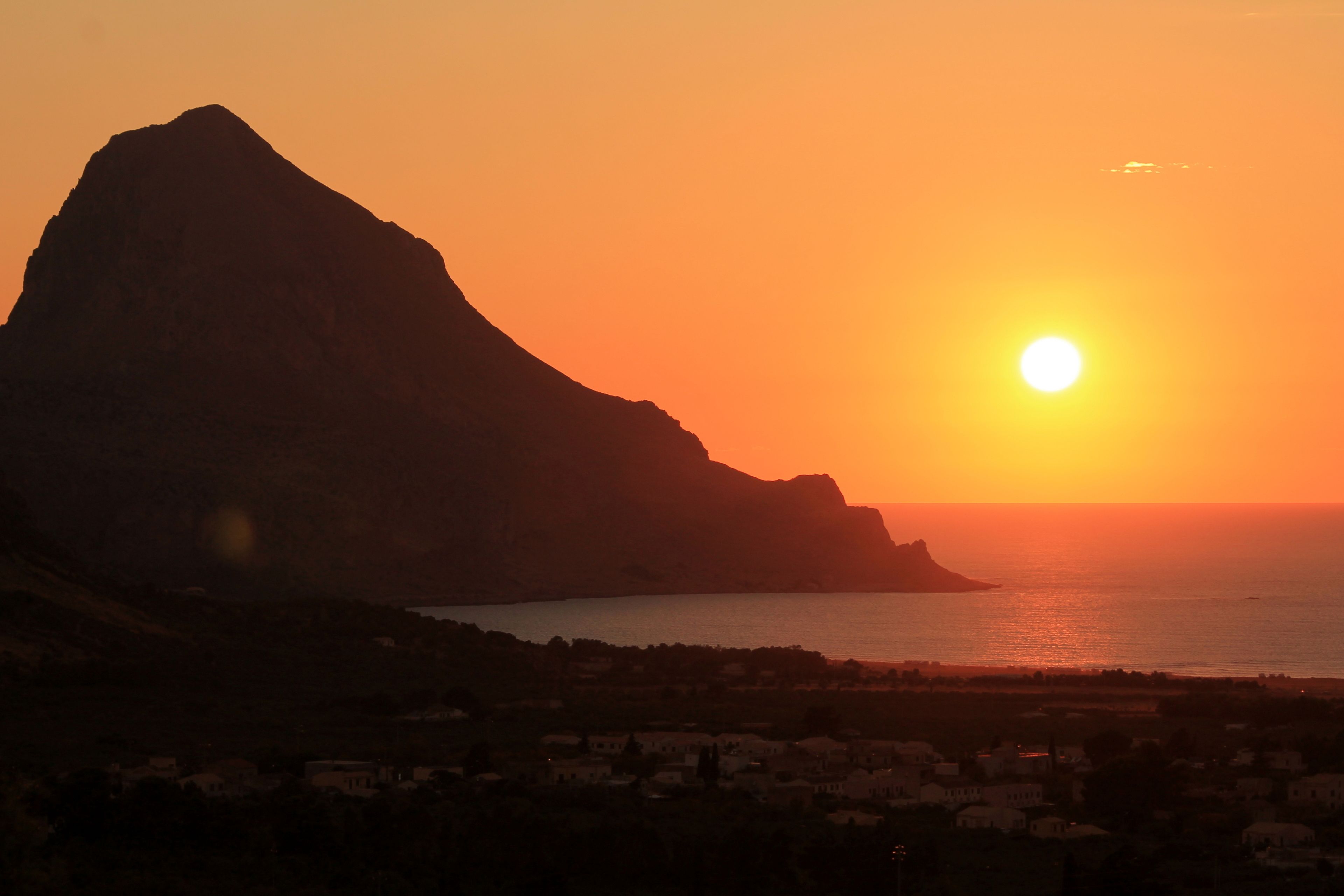 A coastal sunset with a prominent mountain silhouette and a town in the foreground.