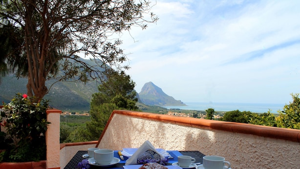 A table with a croissant, two cups, and a napkin on a terrace overlooking a scenic landscape with a mountain and the sea. - Villa Verdesca (San Vito Lo Capo)