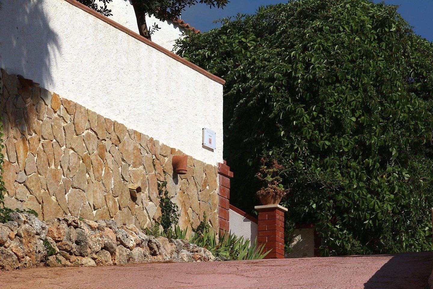 Ein Gebäude mit einer Steinmauer, einer weißen Fassade und einem großen Baum.