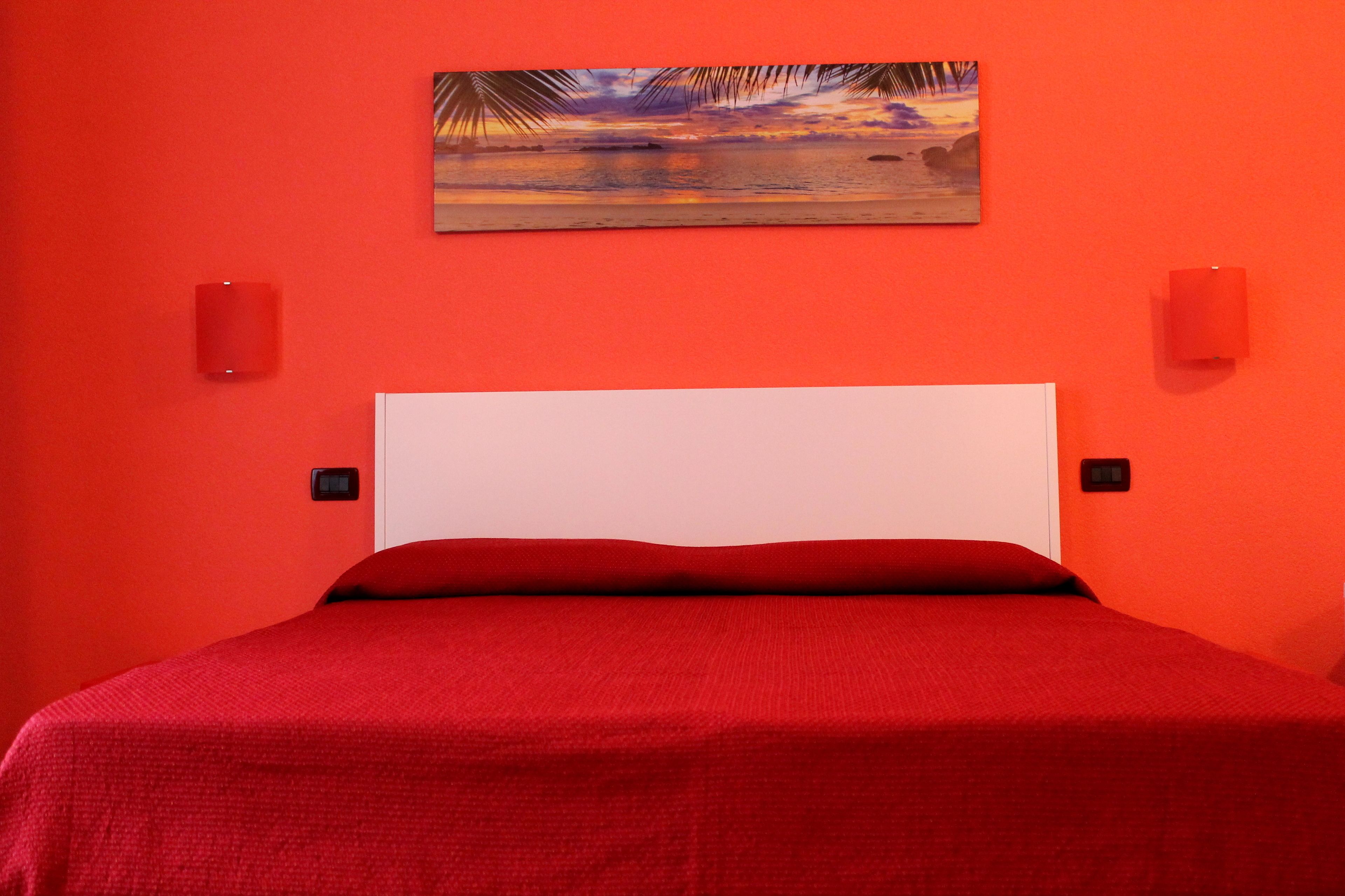 A room with a red wall, a white headboard, and a red bedspread.