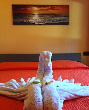 A bed with a red quilt and a painting of a sunset over the ocean on the wall.
