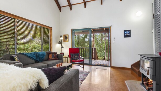 A spacious living room with a sofa, a red chair, a fireplace, and a sliding glass door leading to a balcony.
