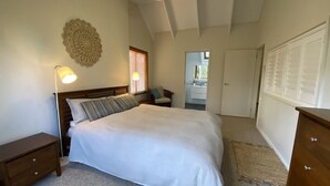 A bedroom with a bed, a nightstand, a lamp, a chair, a wardrobe, and a door leading to another room.