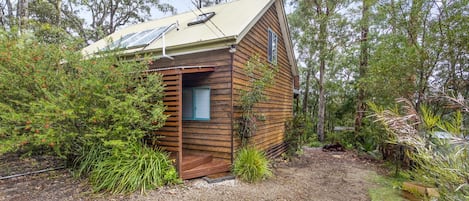 A small wooden cabin with a sloped roof, solar panels, and a small porch.