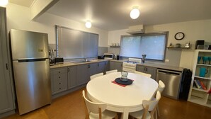 A compact kitchen with a refrigerator, microwave, stove, and sink. There is a dining table with chairs and a clock on the wall.