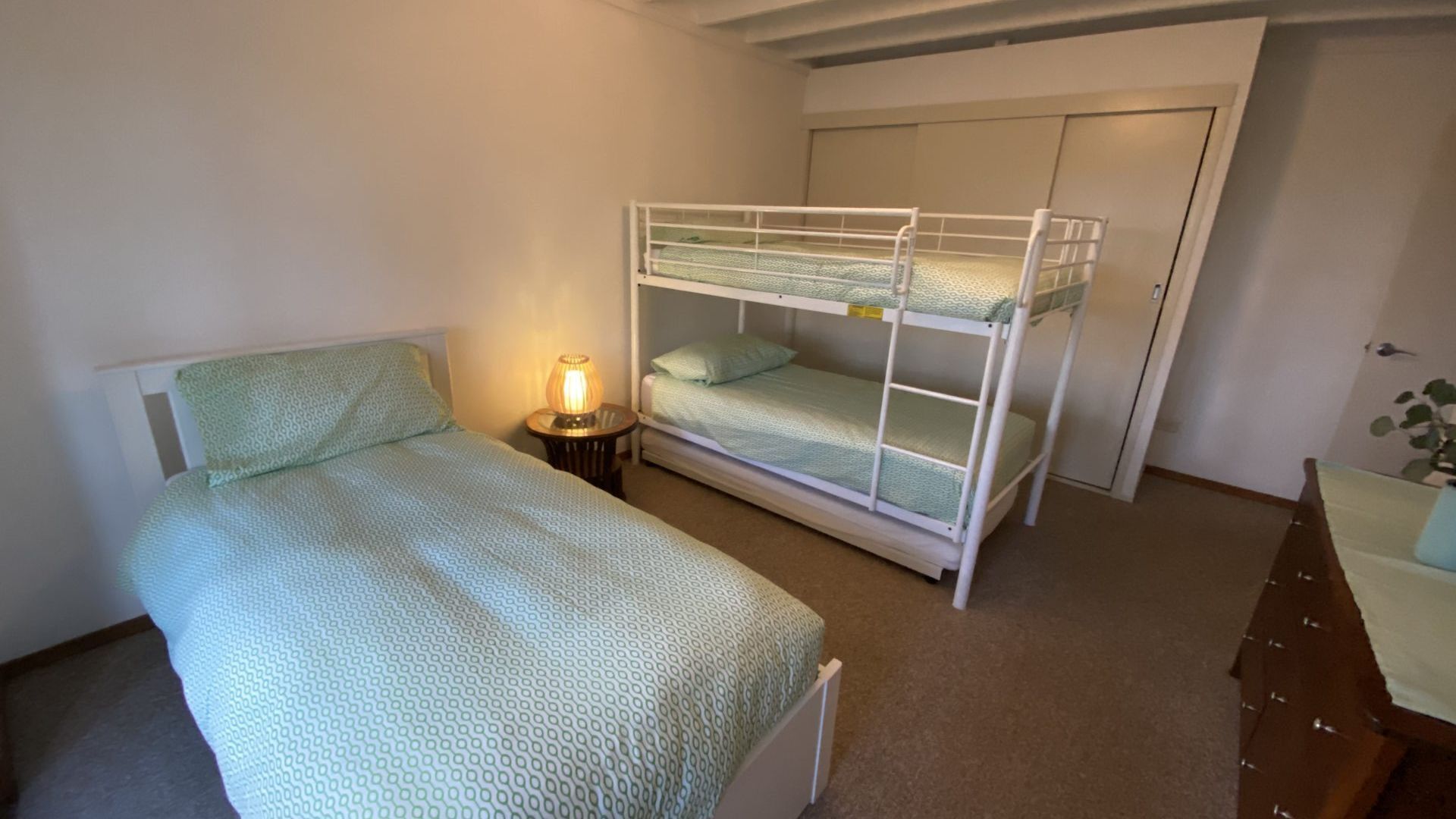 A room with a single bed, a bunk bed, a bedside table with a lamp, and a door.