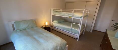 A room with a single bed, a bunk bed, a bedside table with a lamp, and a door.