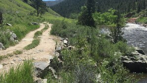 A dirt path leading through a forested area with a river on the right. - Iconic Red House at red house hole! (Bellvue)