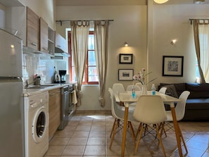 Uma cozinha moderna com máquina de lavar embutida, sala de jantar com mesa e cadeiras, e sala de estar com sofá.