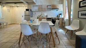 Una cocina moderna con armarios blancos, un comedor con sillas blancas y una escalera que sube a un nivel superior.