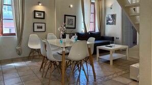 Un comedor con una mesa y sillas blancas, un sofá y una escalera.