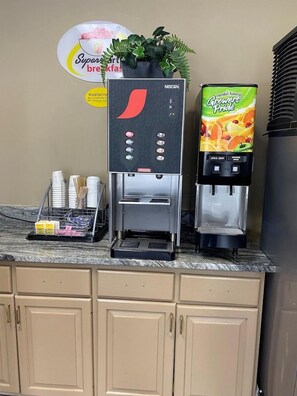 Una kitchenette con una máquina de café Nescafé, un dispensador de jugo y una planta sobre la encimera.