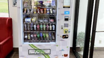 Un distributeur automatique proposant une variété de collations et de boissons, doté d’une interface de paiement et d’une inscription indiquant : « Appuyez ! Vous trouverez de bonnes choses à l’intérieur ! »