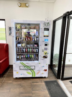 Máquina expendedora con una variedad de aperitivos y bebidas, una interfaz de pago y un letrero que dice '¡Empuja! ¡Hay cosas buenas aquí!'
