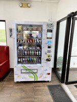 Máquina expendedora con una variedad de aperitivos y bebidas, una interfaz de pago y un letrero que dice '¡Empuja! ¡Hay cosas buenas aquí!'
