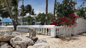 A coastal property with a white fence, palm trees, and a blue-roofed structure. - Beautiful One Bedroom Ocean View Gem (Spring Garden)