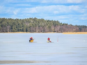 Un lago congelado con dos personas en kayaks, una orilla arbolada y un cielo despejado.