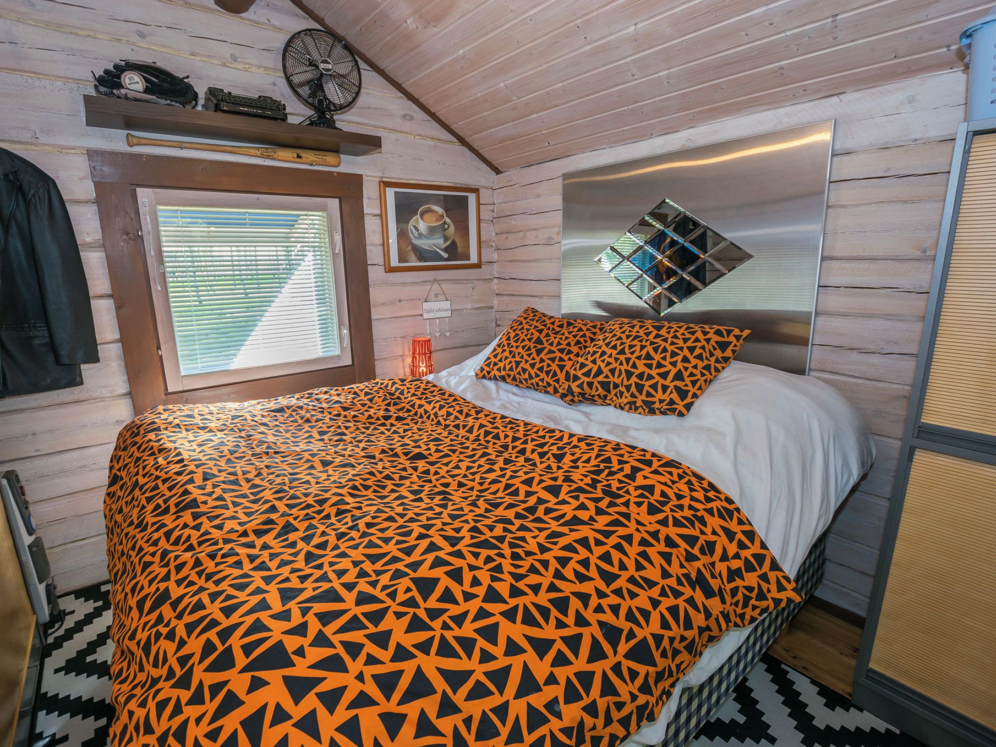 A room with a bed, a window with blinds, a fan, and a mirror on the wall.