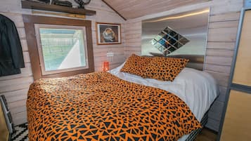 A room with a bed, a window with blinds, a fan, and a mirror on the wall.