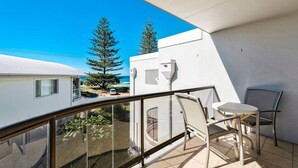 A balcony with a glass railing, two chairs, and a small table. - Ocean Waves - Downtown Oceanfront (Lennox Head)
