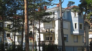 A multi-story building with balconies, surrounded by trees and a fence.