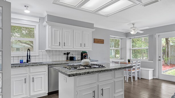 A modern kitchen with white cabinetry, granite countertops, and a central island. There are windows providing natural light and a view of the outdoors. - Private Retreat w/ Pool, Patio, BBQ! 6BR 3BA Gem (Houston)