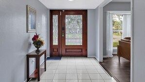 A hallway with a wooden door, a framed picture on the wall, and a small table with a vase of flowers. - Private Retreat w/ Pool, Patio, BBQ! 6BR 3BA Gem (Houston)