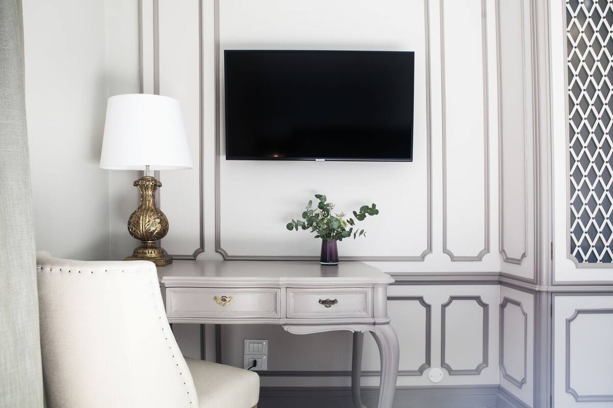 A room with a white desk, a television mounted on the wall, a lamp, and a potted plant.
