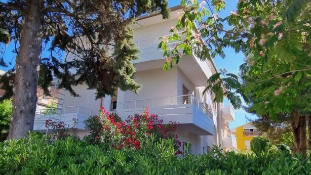 Un edificio de varios pisos con balcones, rodeado de follaje y árboles.