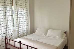 A bedroom with a single bed, white bedding, and a window with patterned curtains.
