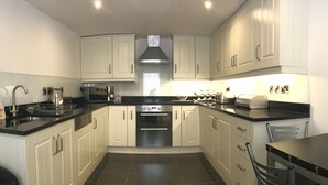 A modern kitchen with white cabinets, black countertops, stainless steel appliances, and a dining area with a table and chairs. - No14 in the heart of St Andrews (St Andrews)