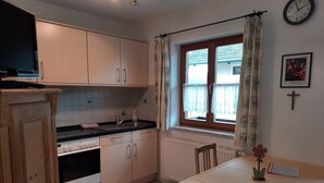 A small kitchen with a dining area, a window with curtains, a clock, and a framed picture on the wall. - Apartment 11 with balcony and terrace, 30 m² (Soyen)
