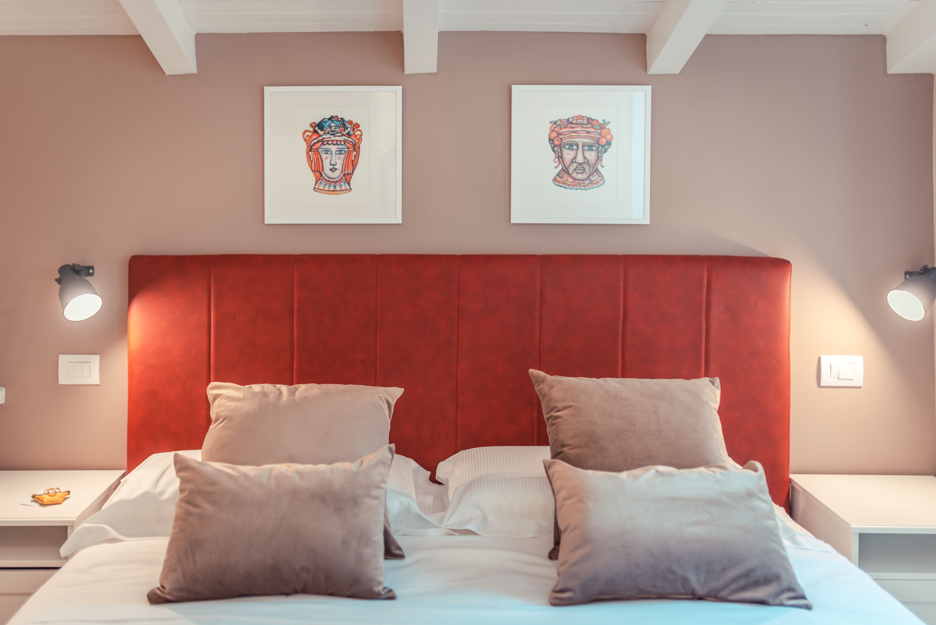 A neatly made bed with a red headboard, white bedding, and multiple pillows. There are two wall-mounted light fixtures on either side of the bed.