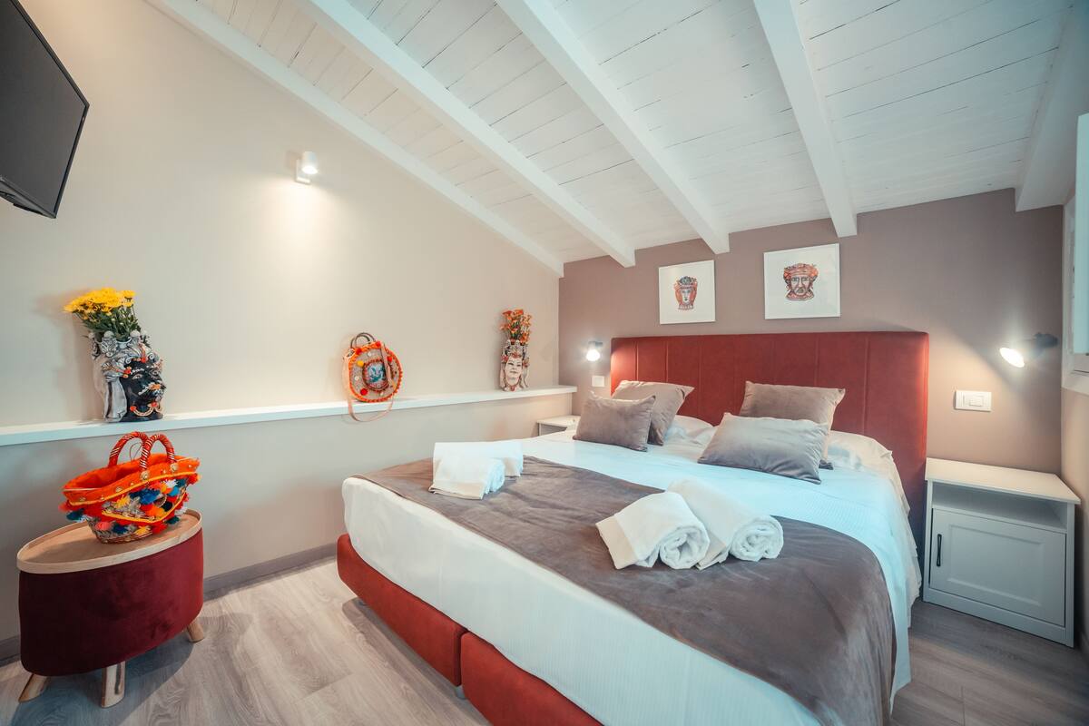 A modern bedroom with a large bed, a red accent wall, and a small side table.