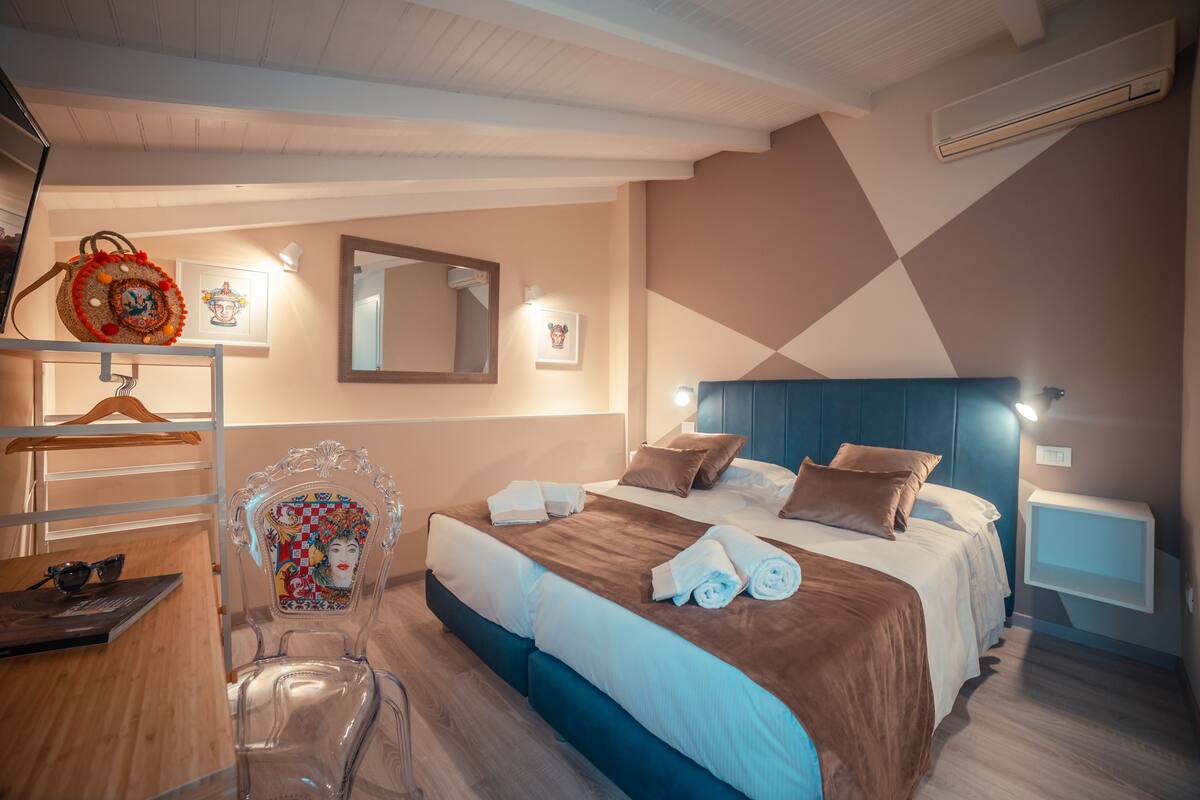 A hotel room with a bed, a desk, a chair, a mirror, and a wall-mounted TV.