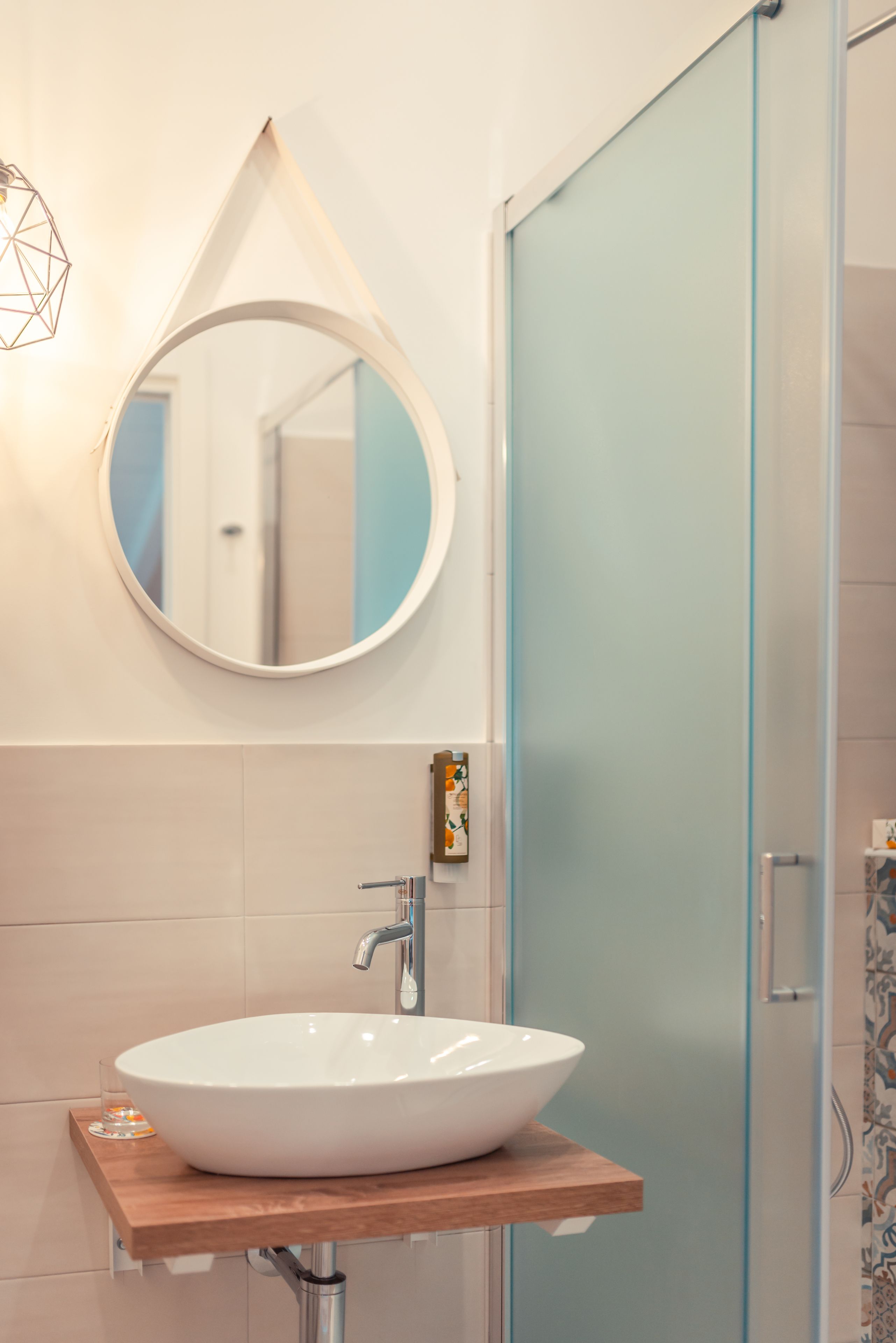 Een badkamer met een witte wastafel, een ronde spiegel en een douchedeur van glas met structuur.