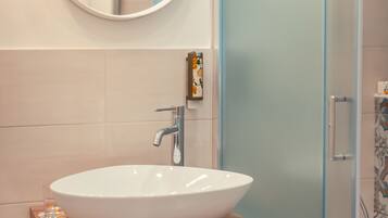 Een badkamer met een witte wastafel, een ronde spiegel en een douchedeur van glas met structuur.